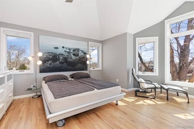 bedroom with vaulted ceiling, multiple windows, baseboards, and light wood finished floors