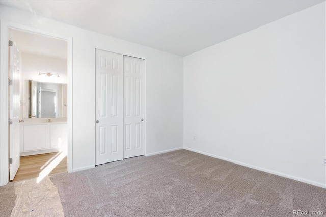 unfurnished bedroom with a closet, light colored carpet, and ensuite bath