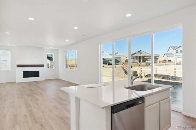 kitchen featuring light wood-type flooring, stainless steel dishwasher, a kitchen island with sink, and white cabinets