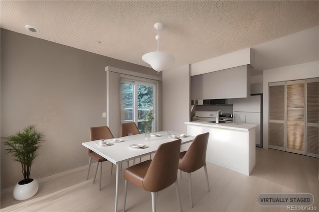 dining space with a textured ceiling, sink, and light hardwood / wood-style flooring