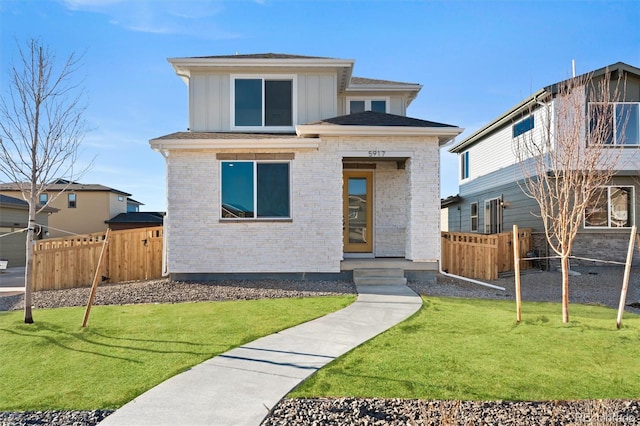 view of front facade with brick siding, a front lawn, fence, and board and batten siding