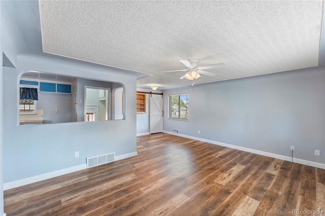 spare room featuring dark hardwood / wood-style floors, a barn door, a textured ceiling, and ceiling fan