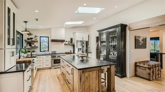 2231 Meadow Green Cir, Franktown, CO 80116 - kitchen featuring appliances with stainless steel finishes, open shelves, dark countertops, light wood finished floors, and a skylight