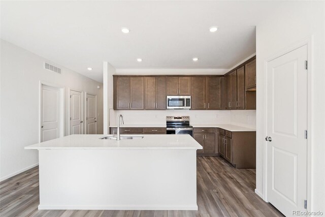 13412 E 110th Way, Commerce City, CO 80022 - kitchen featuring appliances with stainless steel finishes, wood finished floors, a kitchen island with sink, light countertops, and dark brown cabinets