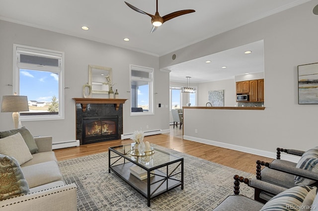 living room featuring light wood-type flooring, baseboard heating, a wealth of natural light, and a tiled fireplace