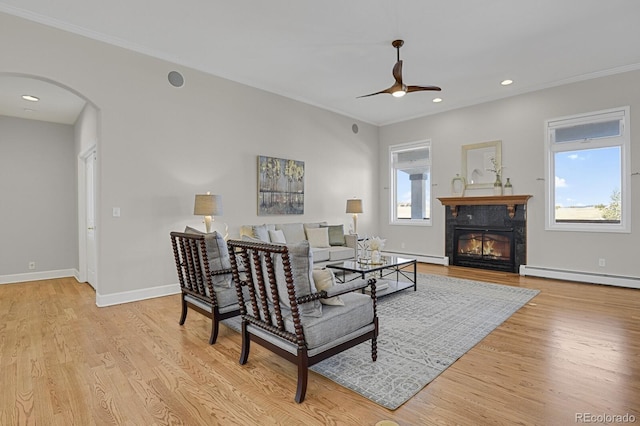 living room featuring arched walkways, a ceiling fan, a glass covered fireplace, wood finished floors, and baseboard heating