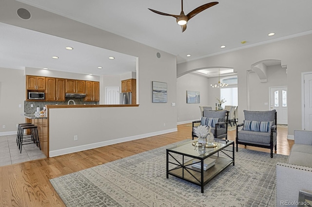 living room with ornamental molding, ceiling fan with notable chandelier, and light wood-type flooring