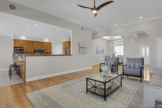 living room with arched walkways, ornamental molding, light wood-type flooring, and baseboards