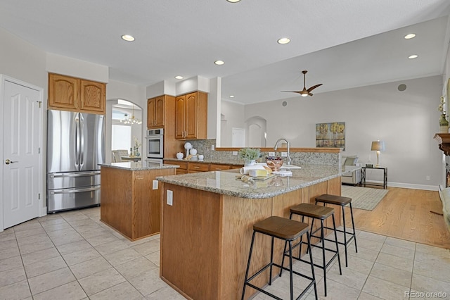 kitchen with a breakfast bar, ceiling fan, light stone countertops, appliances with stainless steel finishes, and a kitchen island