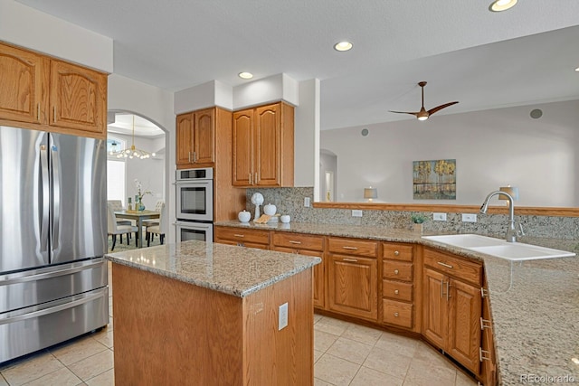 kitchen featuring ceiling fan with notable chandelier, sink, a kitchen island, light stone counters, and stainless steel appliances