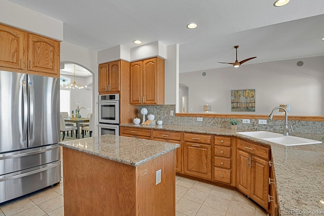 kitchen with arched walkways, light tile patterned floors, a sink, appliances with stainless steel finishes, and light stone countertops