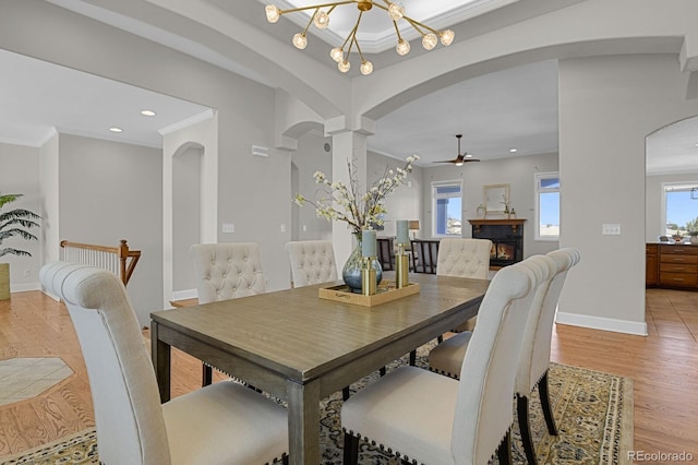 dining area with arched walkways, a wealth of natural light, ornamental molding, a glass covered fireplace, and light wood-style floors