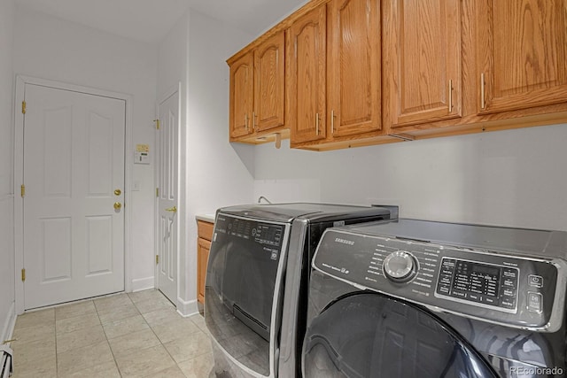 clothes washing area featuring cabinets, light tile patterned floors, and washer and clothes dryer