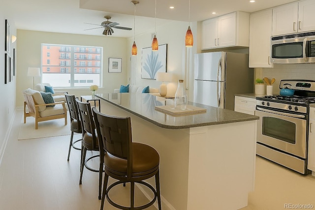1975 Grant St Unit 501, Denver, CO 80203 - kitchen featuring appliances with stainless steel finishes, open floor plan, a ceiling fan, a breakfast bar area, and white cabinets