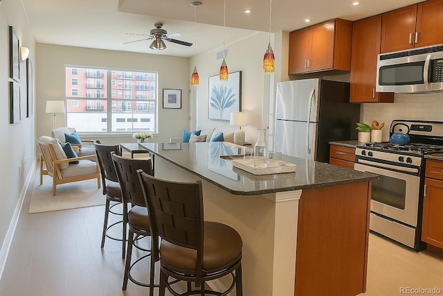 1975 Grant St Unit 501, Denver, CO 80203 - kitchen featuring stainless steel appliances, a ceiling fan, brown cabinetry, a kitchen bar, and backsplash