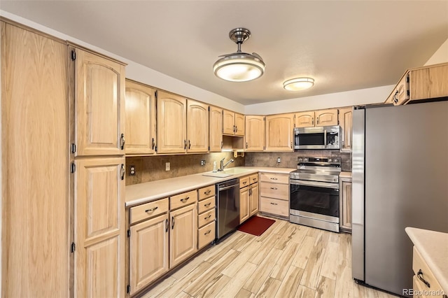 kitchen featuring light countertops, decorative backsplash, light brown cabinetry, appliances with stainless steel finishes, and a sink