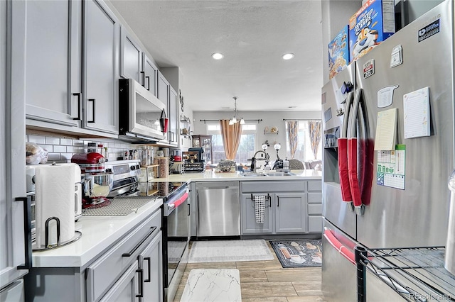 kitchen with stainless steel appliances, gray cabinets, light countertops, decorative backsplash, and a sink