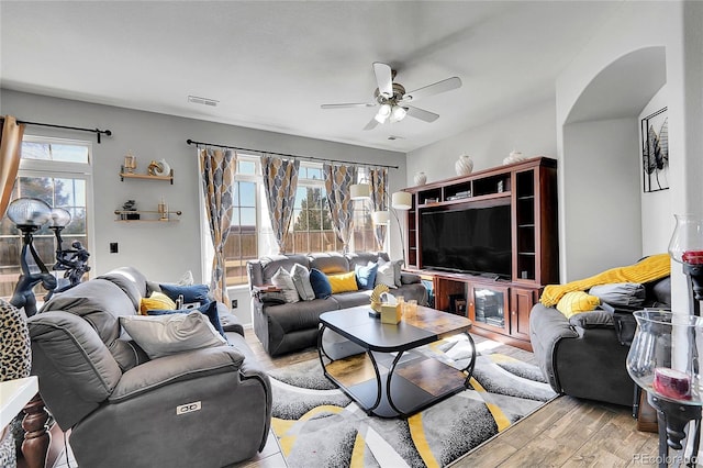 living room with ceiling fan, arched walkways, wood finished floors, and visible vents