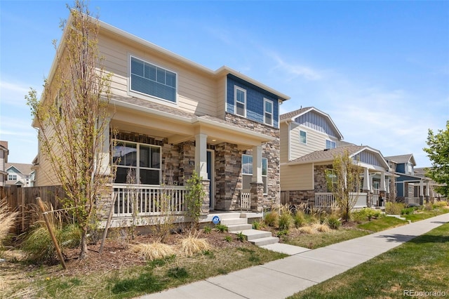 view of front of house with covered porch, stone siding, and fence