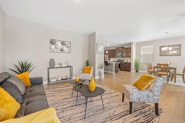living room with a chandelier, light wood finished floors, and baseboards