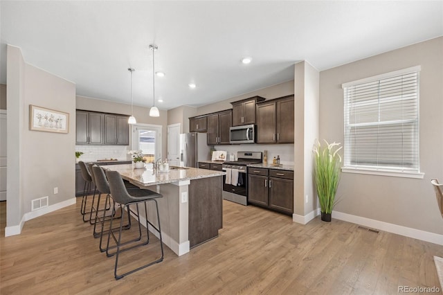 kitchen featuring stainless steel appliances, dark brown cabinets, a breakfast bar, a center island with sink, and light wood-style floors