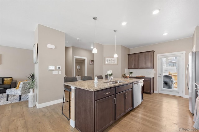 kitchen with stainless steel appliances, a breakfast bar, a center island with sink, light wood-type flooring, and dark brown cabinetry