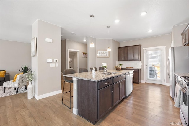 kitchen with a breakfast bar, a center island with sink, dark brown cabinetry, light wood-type flooring, and recessed lighting
