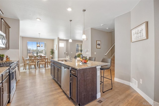 kitchen featuring appliances with stainless steel finishes, a sink, a kitchen breakfast bar, light wood-type flooring, and dark brown cabinets
