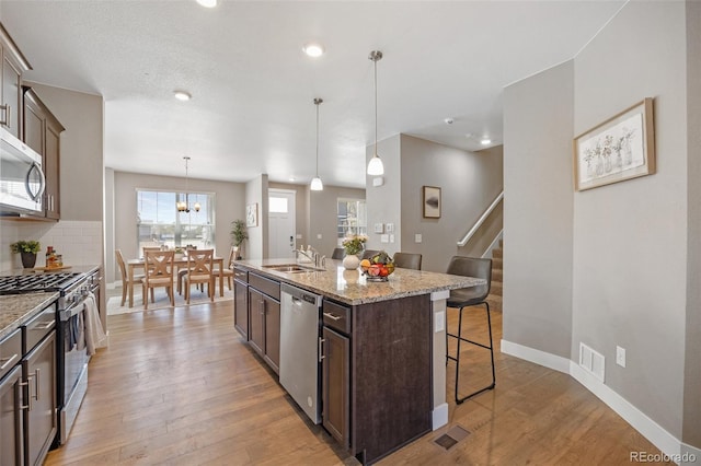 kitchen with appliances with stainless steel finishes, a kitchen bar, dark brown cabinets, a kitchen island with sink, and light wood-type flooring