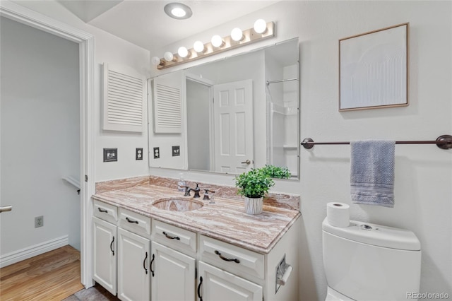 bathroom with toilet, vanity, wood finished floors, and baseboards