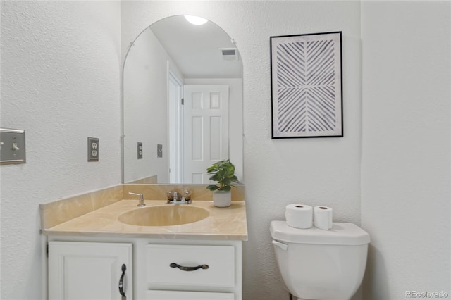 bathroom with toilet, vanity, and a textured wall