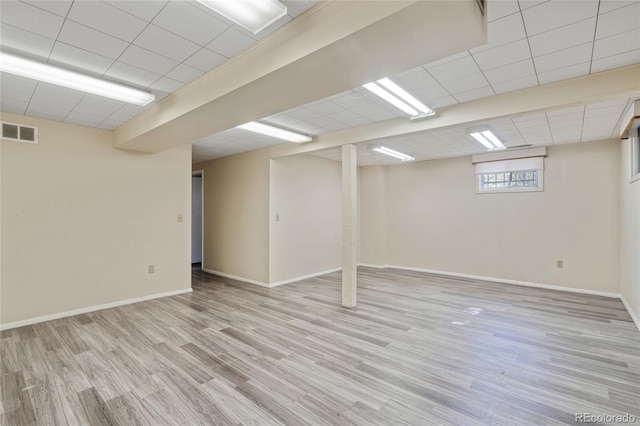 basement with a paneled ceiling, light wood-style flooring, and baseboards