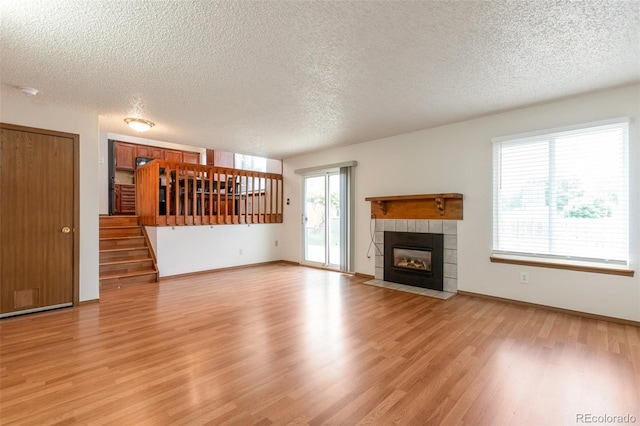 7732 Xavier Ct, Westminster, CO 80030 - unfurnished living room featuring a textured ceiling, light wood-style floors, stairway, a tiled fireplace, and baseboards