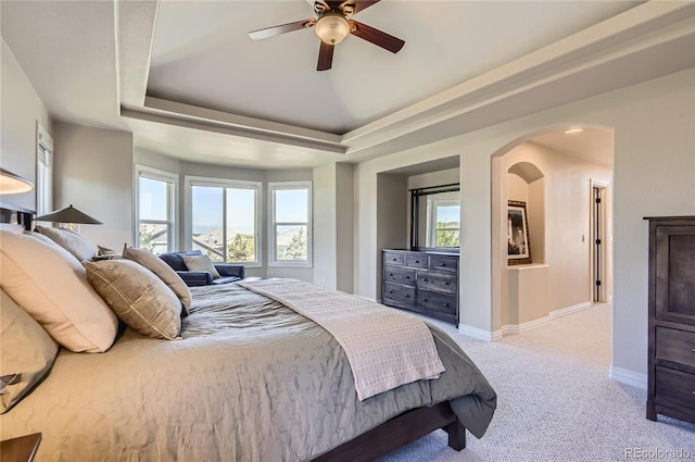 carpeted bedroom featuring multiple windows, arched walkways, baseboards, and a raised ceiling