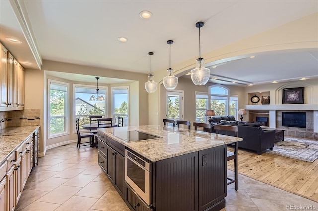 10529 Dacre Pl, Lone Tree, CO 80124 - kitchen with stainless steel microwave, a breakfast bar area, black electric stovetop, recessed lighting, and a glass covered fireplace