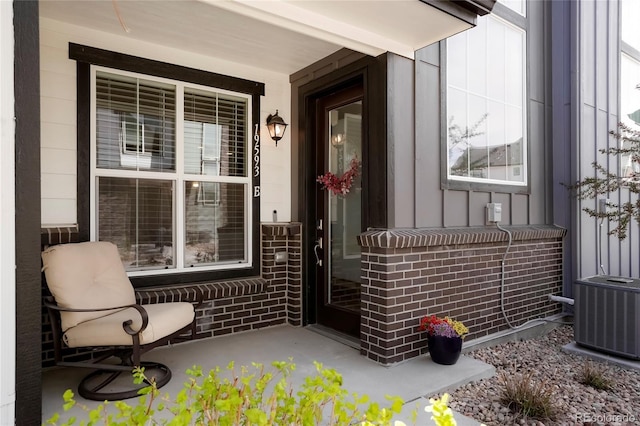 view of exterior entry featuring central AC, board and batten siding, a porch, and brick siding