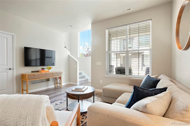living room featuring baseboards, stairway, visible vents, and wood finished floors