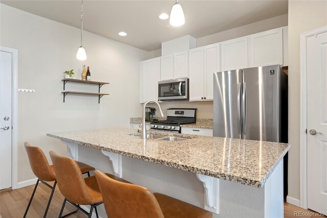 kitchen featuring a breakfast bar area, a sink, white cabinetry, open shelves, and appliances with stainless steel finishes