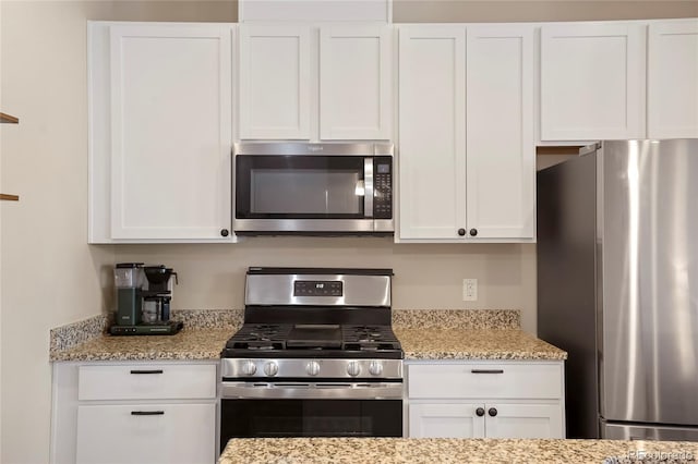 kitchen with light stone countertops, stainless steel appliances, and white cabinets