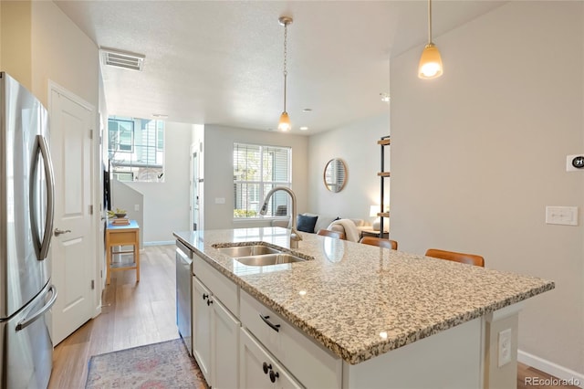 kitchen with a sink, white cabinets, light wood-style floors, stainless steel appliances, and a kitchen island with sink