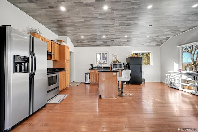 kitchen featuring a kitchen island, appliances with stainless steel finishes, lofted ceiling, a breakfast bar area, and light hardwood / wood-style flooring