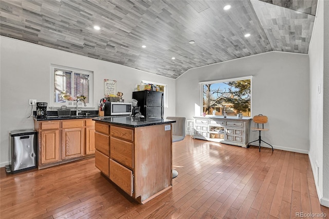 kitchen with a kitchen island, black refrigerator, lofted ceiling, sink, and hardwood / wood-style flooring