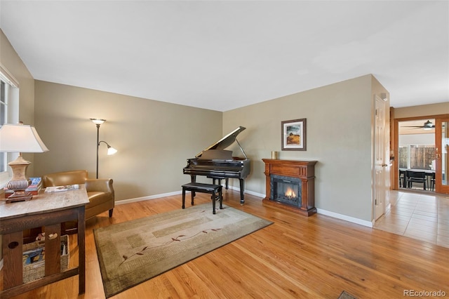 living area with a glass covered fireplace, a ceiling fan, baseboards, and wood finished floors