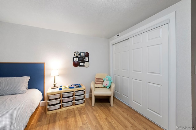 bedroom featuring light wood finished floors, visible vents, baseboards, a closet, and a textured ceiling