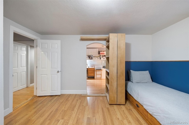 bedroom featuring arched walkways, light wood-style flooring, a textured ceiling, and baseboards