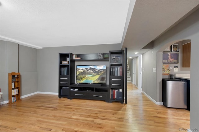 living room with light wood-type flooring, baseboards, and arched walkways