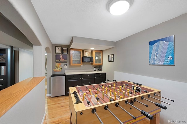 playroom featuring baseboards, arched walkways, a textured ceiling, and light wood-style flooring