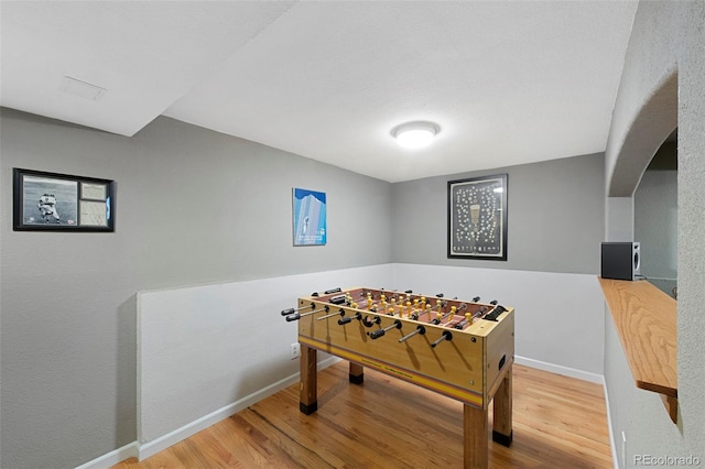 recreation room featuring arched walkways, baseboards, and wood finished floors