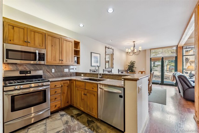 kitchen with appliances with stainless steel finishes, a sink, a peninsula, decorative backsplash, and a chandelier