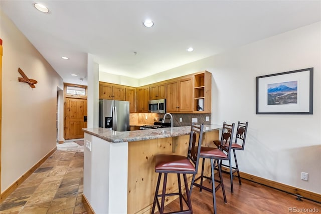 kitchen with stainless steel appliances, open shelves, baseboards, a peninsula, and light stone countertops
